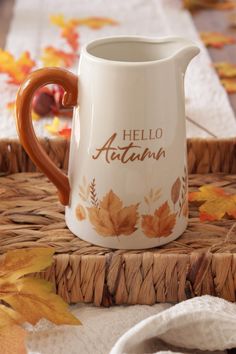 a ceramic pitcher with the words hello autumn painted on it sitting on a wicker tray