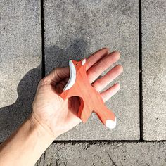 a hand holding an orange and white object in it's left hand on concrete