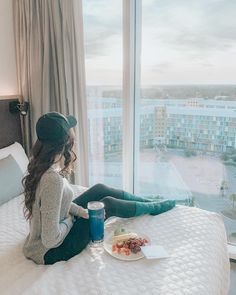 a woman sitting on top of a bed with a plate of food in front of her