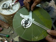 a man is working on a green clock with metal parts around him and tools nearby