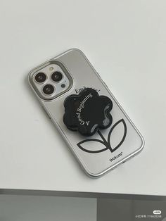 an iphone case with a black flower on the front and back cover, sitting on a white surface