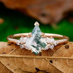 a green and white diamond ring sitting on top of a leaf