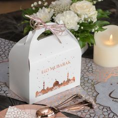 a white box sitting on top of a table next to a candle and some flowers