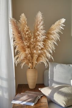 a plant in a vase sitting on a table next to a book and pillow with a window behind it