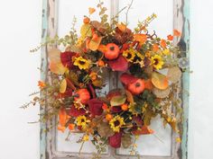 a wreath is hanging on the front door with autumn flowers and leaves in oranges, yellows and browns