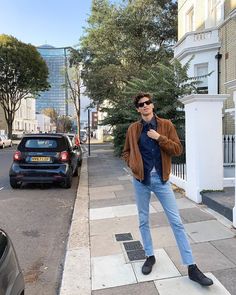 a man is standing on the sidewalk in front of some parked cars and wearing sunglasses