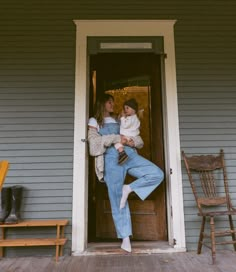 a woman holding a baby in her arms while standing on the front porch of a house