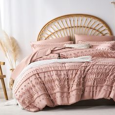 a bed with pink comforter and pillows in a room next to a wicker headboard