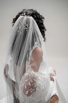 the back of a bride's veil with flowers and pearls on it, as she sits in a chair