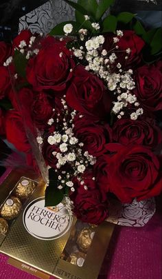 a bouquet of red roses and white flowers in a vase next to a box of chocolates