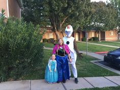 two children and an adult standing in front of a house with a large frosty the snowman costume on