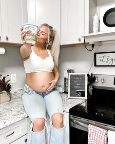 a pregnant woman sitting on top of a kitchen counter holding up a can of food