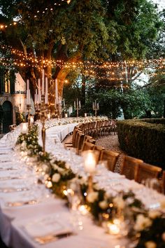 a long table set up for an event with lights strung from the trees and greenery