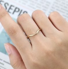 a woman's hand with a gold ring on top of her finger, reading the newspaper