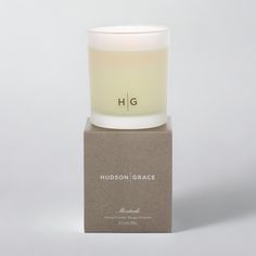 a white candle sitting on top of a wooden block next to a cardboard box with the words hudson grace printed on it