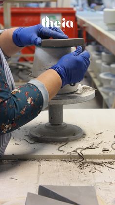 a woman working on a piece of metal with blue gloves and other items in the background