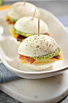 two eggs and bacon sandwiches on a white plate with toothpicks in the middle