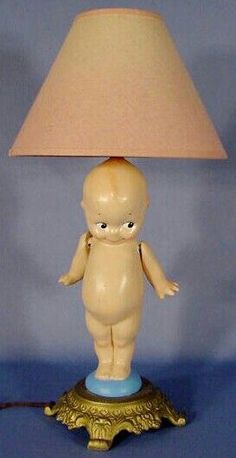 a lamp that has a little baby doll on it with a pink shade over the base