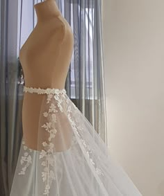 the back of a wedding dress on display in front of a window with sheer curtains