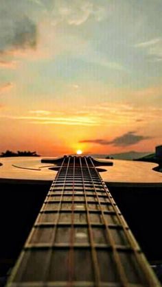 the sun is setting over an electric guitar neck in front of a body of water