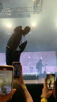 a man standing on top of a stage while holding up his cell phones in front of him