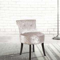 an upholstered chair in front of a white brick wall with a lamp next to it