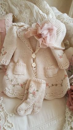 a knitted sweater and booties laying on top of a white bed next to pink flowers