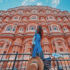 a woman wearing a blue jacket and hat walking past a tall pink building with ornate balconies