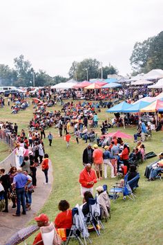 a crowd of people standing around tents on top of a grass covered field next to trees