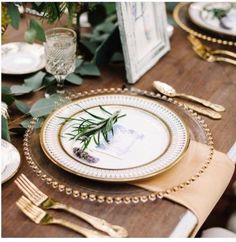 the table is set with gold and white plates, silverware, and greenery