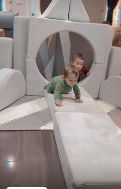 two small children are playing in a play area with white walls and grey carpeting