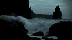 waves crashing against the rocks at night near an ocean shore with dark cliffs in the background