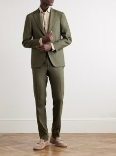 a man in a green suit standing on a hard wood floor with his hands together