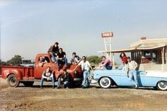 a group of people sitting on the back of an old truck in front of a gas station