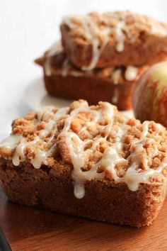 two pieces of bread with icing sitting on top of a cutting board next to an apple