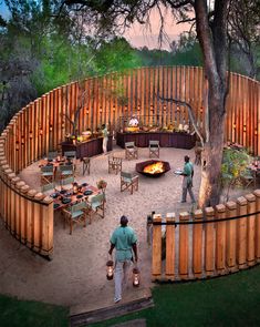 two men standing in front of a fire pit surrounded by wooden fenced area with chairs and tables