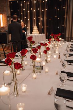 a long table with candles and red roses in vases on the tables are set for a formal function