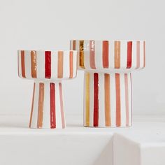 three striped vases sitting on top of a white shelf with red, orange and yellow stripes