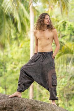 a shirtless man standing on top of a rock in the jungle with trees behind him