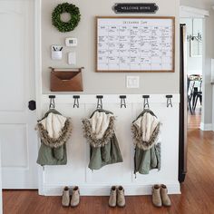 three coats hanging on the wall in front of a calendar and coat rack with four pairs of shoes