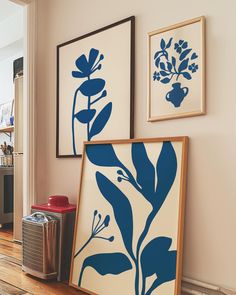 two blue and white paintings hanging on the wall next to a trash can in a living room