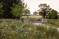 a stone gate in the middle of a field with wildflowers and trees around it