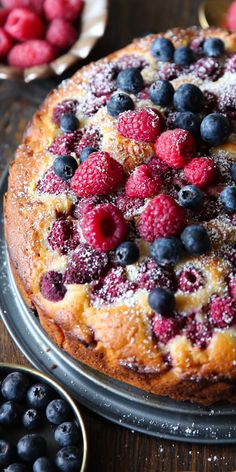 a cake topped with berries and powdered sugar on top of a metal pan next to blueberries