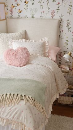 a white bed topped with pillows and a pink heart shaped pillow on top of it