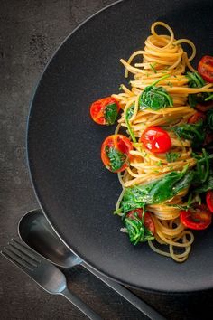 pasta with tomatoes and spinach on a black plate