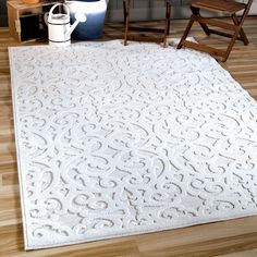 a large white rug on top of a hard wood floor next to a wooden chair