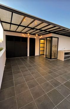 an empty patio with black garage doors and lights hanging from the ceiling, in front of a white building