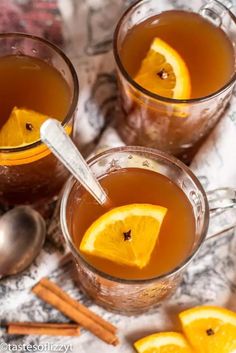 two mugs of tea with orange slices and cinnamon sticks