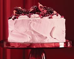 a cake with white frosting and berries on top sitting on a glass platter