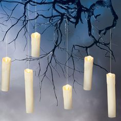 five candles hanging from strings in front of a tree with branches and moon behind them